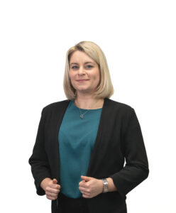 Elegantní žena v černém s modrou blůzou a hodinkami, portrét na bílém pozadí, profesionální vzhled, vhodné pro obchodní nebo pracovní prostředí.